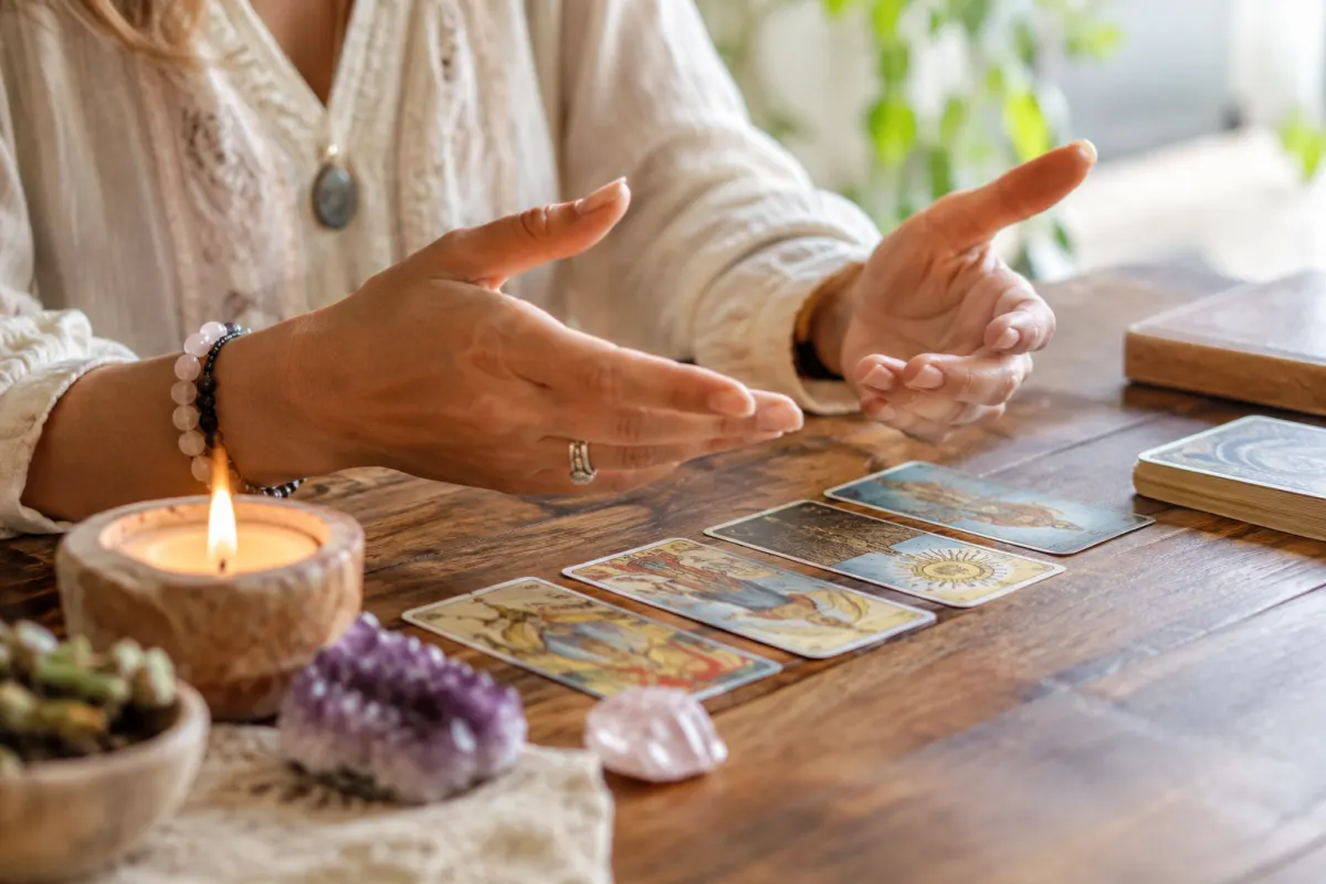 Ma guidance spirituelle : éclairer son chemin sans prédire l'avenir Gros plan sur les mains d'une praticienne tenant un pendule au-dessus d'un jeu de cartes de tarot